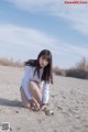 A woman kneeling on a sandy beach with her legs crossed.