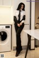 A woman in a white shirt and black tie standing next to a washing machine.