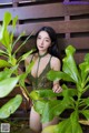 A woman in a green lingerie posing in front of a plant.