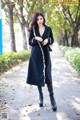 A woman in a black coat is walking down a sidewalk.